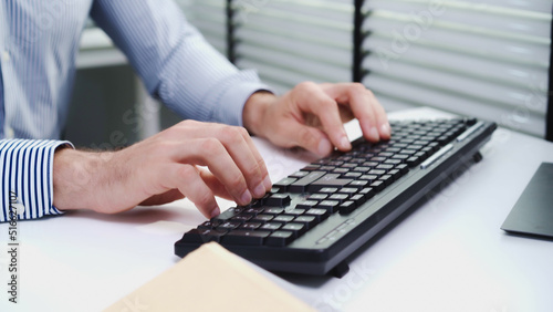 Close-up or closeup shot of Caucasian male employee's hand typing on keyboard to work with business agreement at his office table. White businessman with leadership skill negotiating with customers.