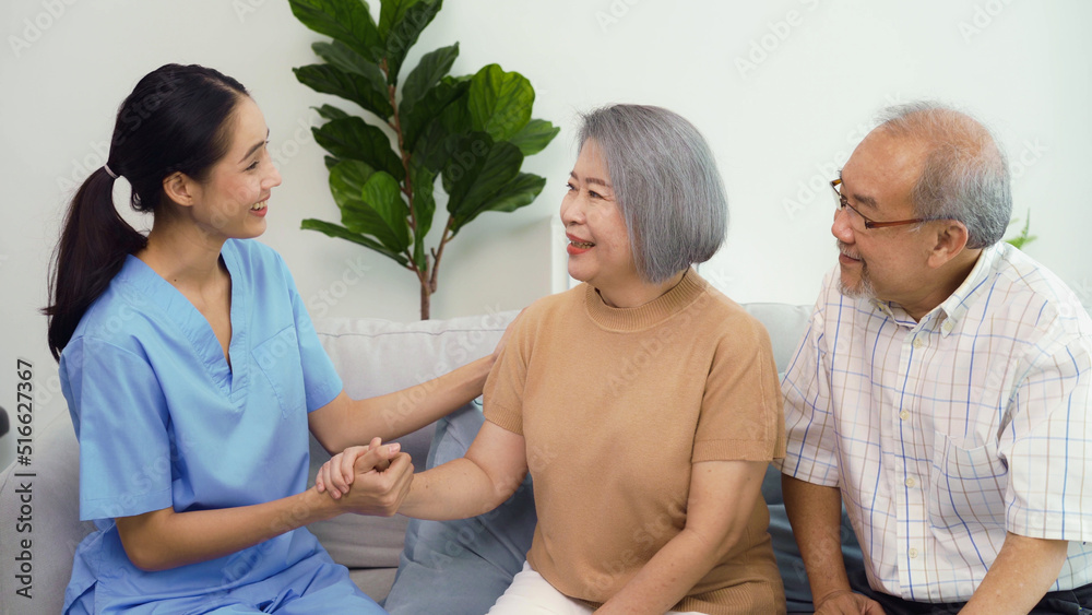 Obraz premium Portrait of Asian senior grandparents and young nurse home care sitting on sofa and talking together. Shot of female caregiver with smile face holding hand of grandmother. Health care at home concept