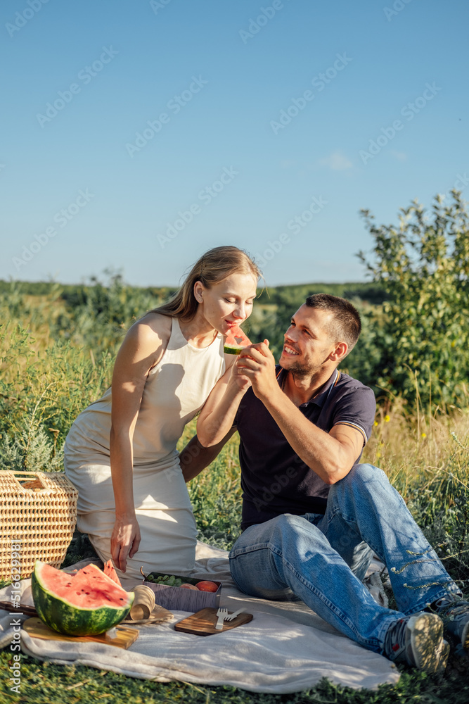 Happy flirting loving couple kissing and having date outdoors. Young couple on summer picnic with watermelon.