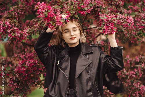 Bright fresh portrait of a young happy blonde girl in black on the backdrop of pink flower tree in autumn as wallpaper, background, magazine cover, poster or advertising design.  photo