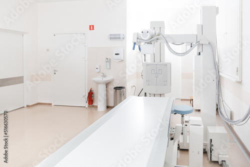 X-ray department in modern hospital. Radiology room with scan machine with empty bed. Technician adjusting an x-ray machine. Scanning chest, heart, lungs in modern clinic office. © Maksim