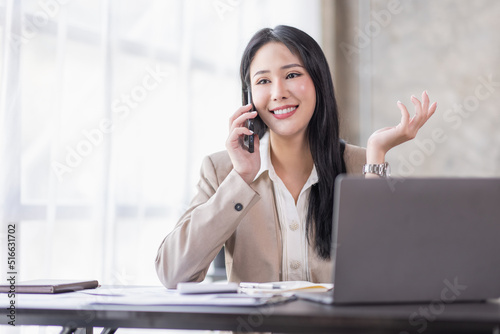 Asian businesswoman working at home with a laptop and talking on smartphone 