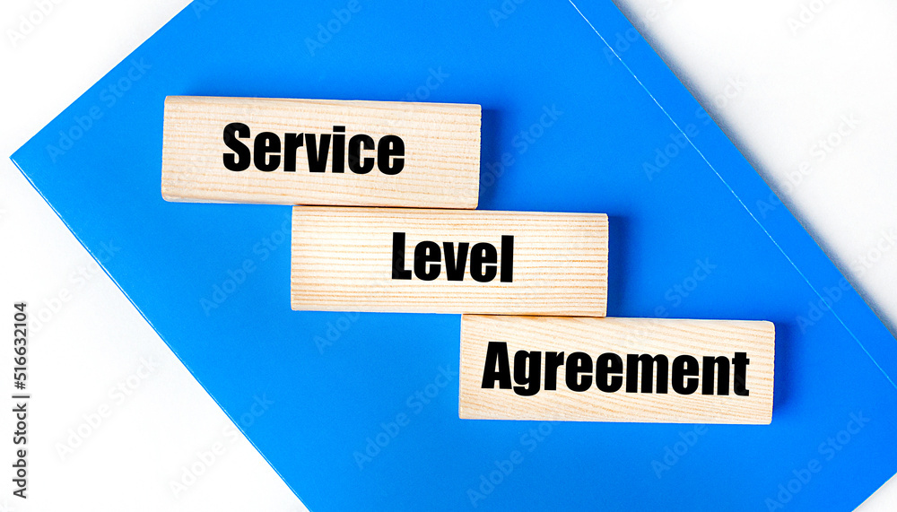 There is a blue notebook on a light gray background. Above are three wooden blocks with the words SLA Service Level Agreement There is a blue notebook on a light gray background. Above are three wooden blocks with the words SLA Service Level Agreement