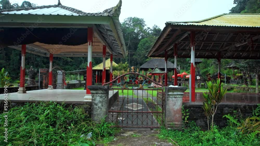 Indonesian temple standing in a field near a forest with an iron gate