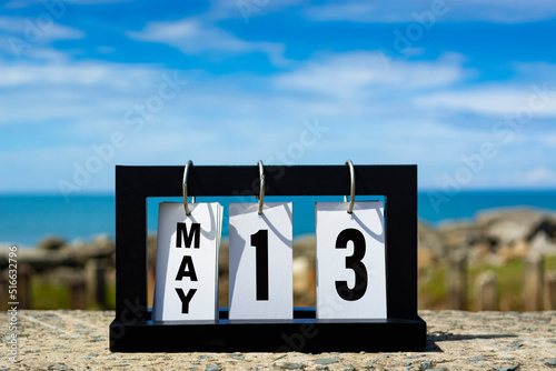 may 13 calendar date text on wooden frame with blurred background of ocean.
