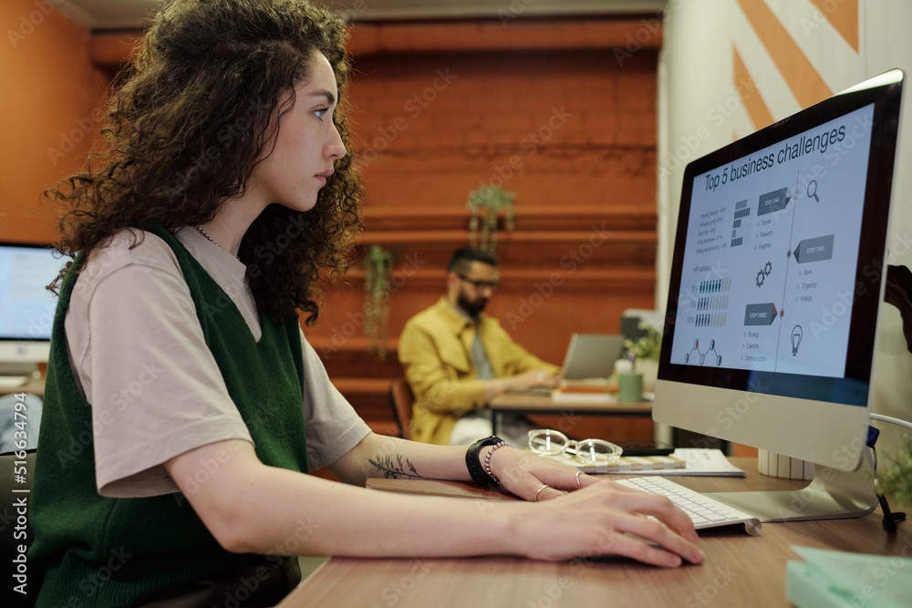 Young serious businesswoman analyzing finnacial data on computer screen while sitting by workplace in front of monitor in office Young serious businesswoman analyzing finnacial data on computer screen while sitting by workplace in front of monitor in office