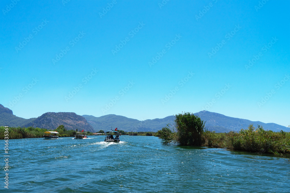 Tourist pleasure boat on Dalyan River, next to rocks, which contain Lycian tombs, in Mugla Province located between districts of Marmaris and Fethiye on south-west coast of Turkey Tourist pleasure boat on Dalyan River, next to rocks, which contain Lycian tombs, in Mugla Province located between districts of Marmaris and Fethiye on south-west coast of Turkey