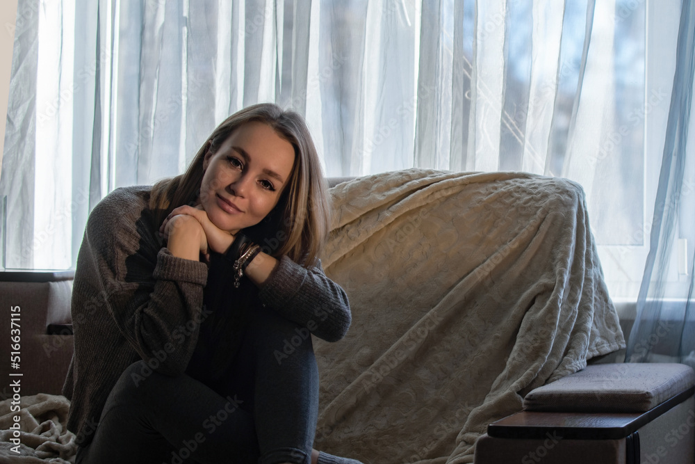 portrait of a beautiful young woman in comfortable home clothes on the sofa at home against the background of the window portrait of a beautiful young woman in comfortable home clothes on the sofa at home against the background of the window