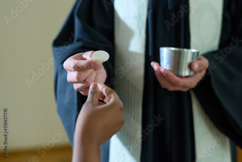 фотографія Hand of young female parishioner taking unleavened bread held by Catholic priest