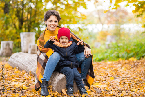 Mother and little son spend time together in the autumn park. The boy makes a threatening face, tries to scare and looks at the camera