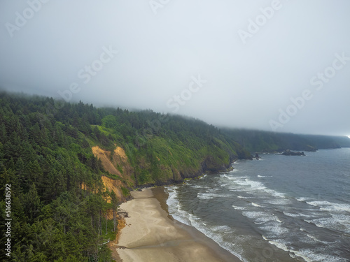 Mountain range covered with pine forest near the sandy shore of the ocean. Light white waves and ripples on the water. Beautiful seascape. There are no people in the photo. Banner, postcard.