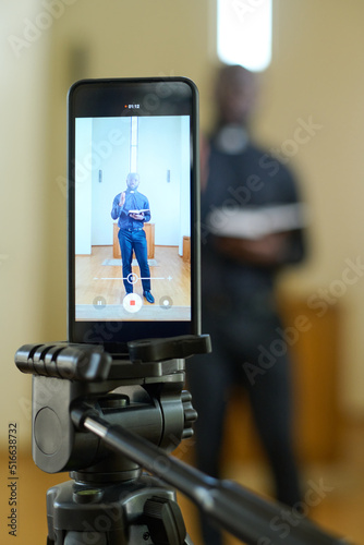 Screen of smartphone with pastor holding open Bible while standing in front of wooden pulpit and preaching during church service