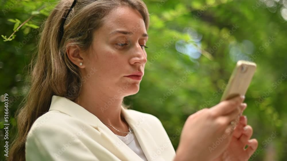 Woman wearing white business suite working on mobile phone in a park Woman wearing white business suite working on mobile phone in a park