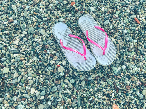 hot, tropical country with sea and mountains. on the beach there are pebbles and small stones. on the ground are white women's slippers for walking