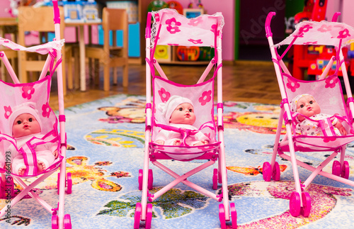 Three dolls are sitting in pink toy carriages. Playroom in kindergarten photo