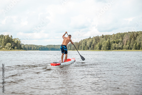 Paddling on a SUP board on a lake at sunny day. Stand up paddle boarding - awesome active outdoor recreation.