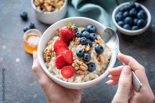 Oatmeal porridge bowl with berry fruits in female hands, closeup view. Healthy vegetarian breakfast food