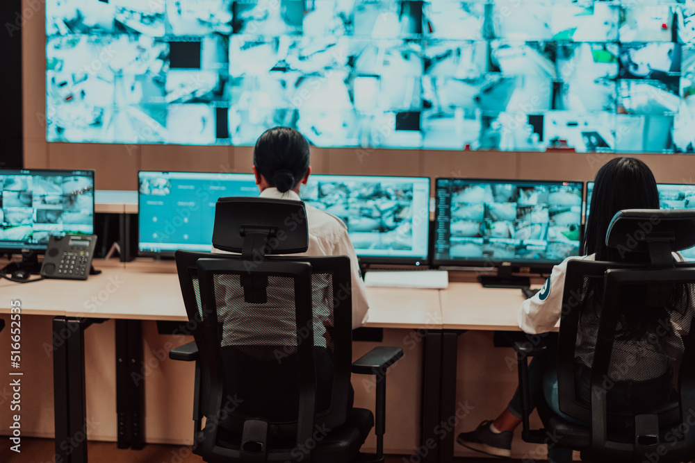 Group of Security data center operators working in a CCTV monitoring room looking on multiple monitors Officers Monitoring Multiple Screens for Suspicious Activities Team working on the System Contr Group of Security data center operators working in a CCTV monitoring room looking on multiple monitors Officers Monitoring Multiple Screens for Suspicious Activities Team working on the System Contr