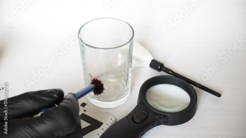 Professional criminologist in black gloves taking fingerprints from glass by special brush, job. White background, man's hands photo