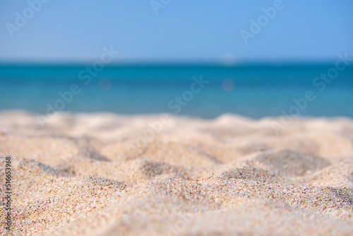 Close up of clean yellow sand surface covering seaside beach with blue sea water on background. Travel and vacations concept