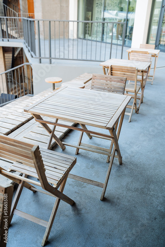 Outdoor cafe with wooden tables, wooden furniture, folding garden furniture, city catering place, have a snack at the table. © Aleksey