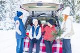 four children friends boys and girl teenagers traveling and having fun in trunk car in snow winter forest, drinking tea from thermos, talking and get ready to celebrate Christmas or New year together