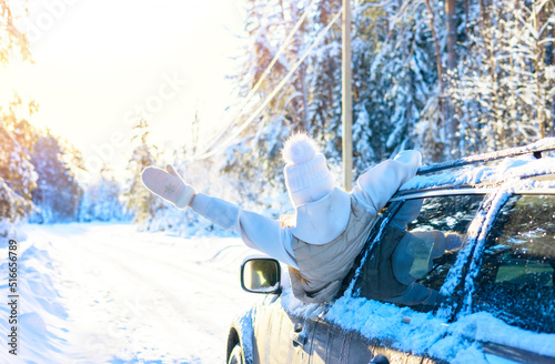 teenage girl in white sweater, vest and white knitted hat in car window in snowy forest having fun, concept of winter local travel during Christmas or New Year holidays and vacations