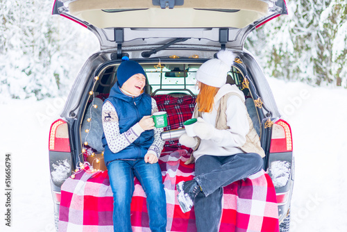 two children friends boy and girl teenagers traveling and having fun in trunk car in snow winter forest, drinking tea from thermos, talking and get ready to celebrate Christmas or New year together