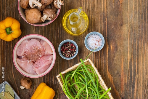 Prepared ingredients for cooking chicken stew with mushrooms  sweet peppers and garlic arrows on a wooden background. seasonal recipes.