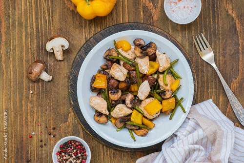 Chicken stew with mushrooms, sweet peppers and garlic arrows in a gray plate on a wooden background.