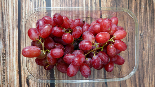 pink grapes in a plastic container stand on a brown wooden table.view from above. grona grapes photo