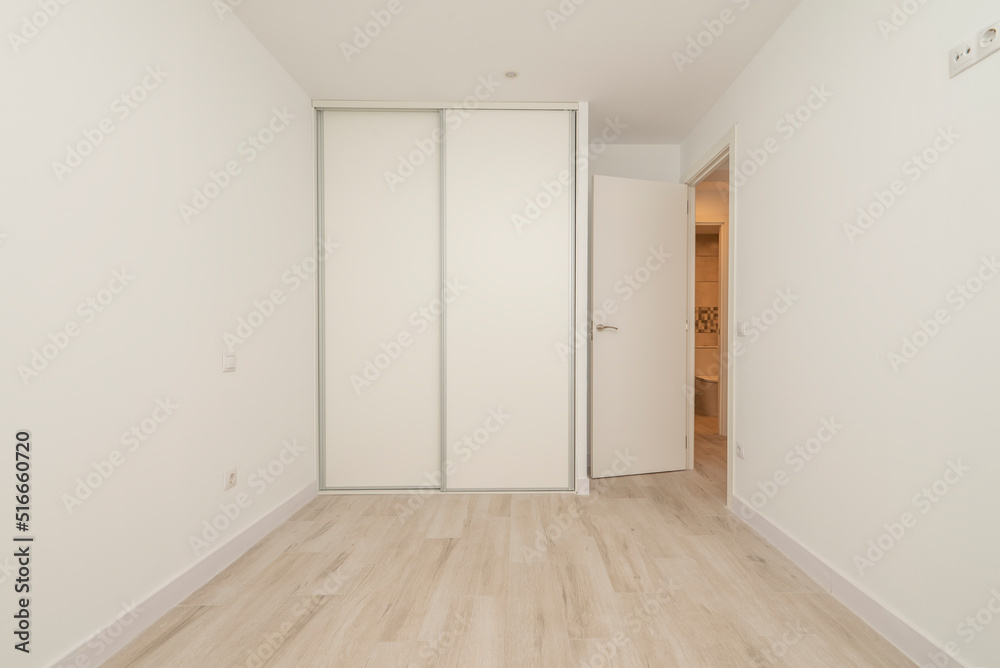 Fototapeta premium Empty bedroom with light wood flooring, plain white painted walls and built-in wardrobe with white sliding doors