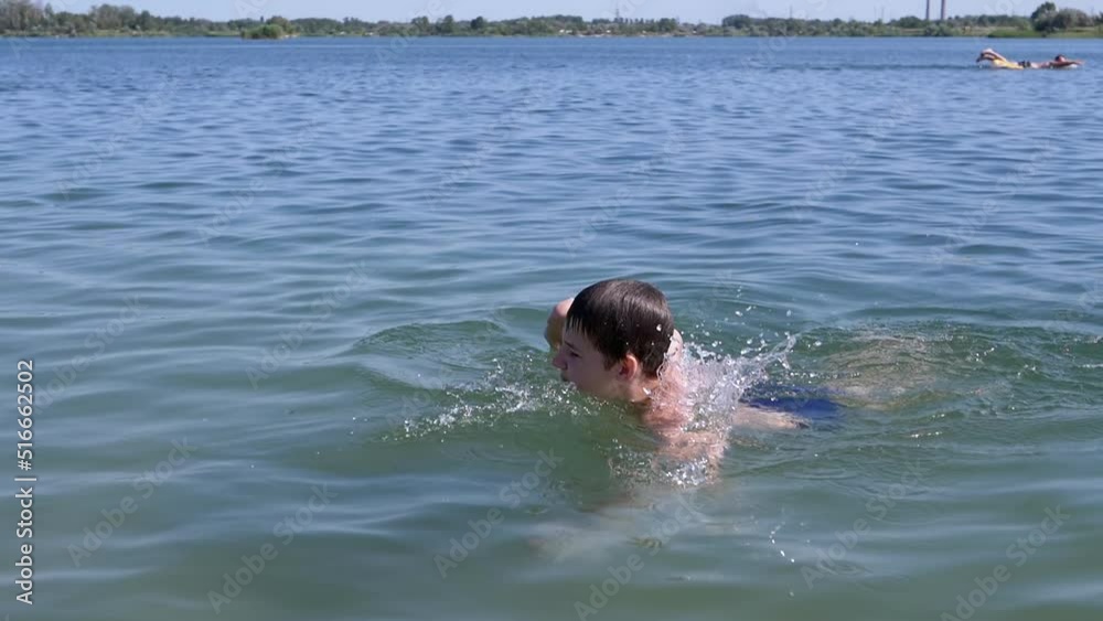 Happy Child Swimming, Diving, Holds Breath Underwater on Blue Water in Sunrays. A boy learns to swim freestyle on beach. Sports training. Health. Rest, recuperation, summer family vacation. Lifestyle.