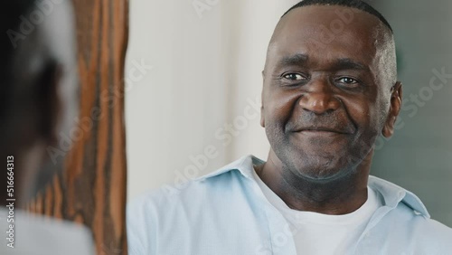 Close up portrait mirror reflection happy senior retired african adult american man with bristle smiling wink himself stand in dressing room planning date makes thumb up hand gesture feels confidence