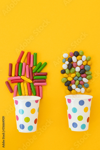 Paper cups with tasty candies on color background