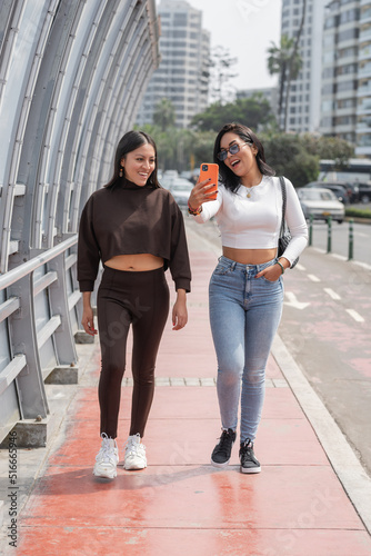 Vertical photo of two friends taking a selfie while walking on the street