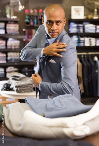 Confident young man looking for jacket in mens clothing boutique
