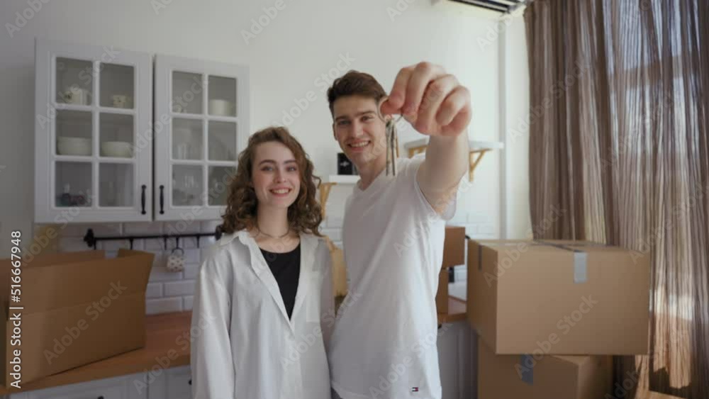Happy couple comes to countertop in kitchen showing key to new apartment at camera. Man and woman feel happy with successful purchase from third party to POV Happy couple comes to countertop in kitchen showing key to new apartment at camera. Man and woman feel happy with successful purchase from third party to POV