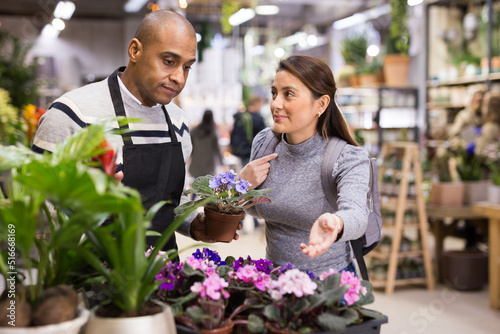 Shop assistant helping woman to choose geranium flowers in flower shop
