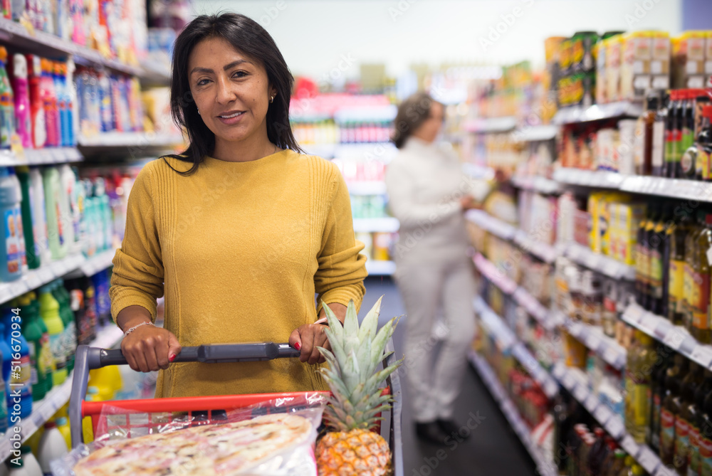 Woman shopping at store, walking among shelves and choosing products