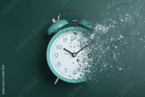 Time is running out. Turquoise alarm clock vanishing on green background, top view