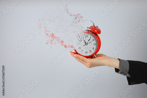Time is running out. Woman holding vanishing red alarm clock against light grey background, closeup