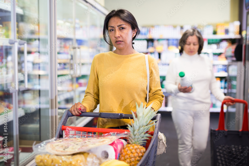 Positive woman choosing food products on shelves in grocery shop