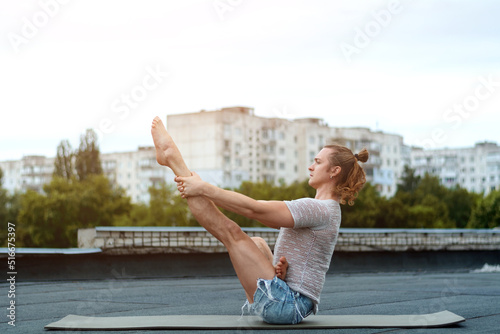 A man practices yoga on the roof of the house. Yoga at sunset. Healthy life, sport and meditation concept.