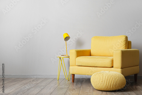Canvastavla Comfortable armchair with table, lamp and ottoman near light wall in room