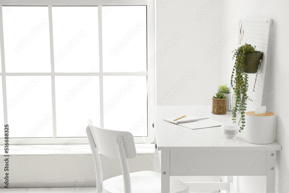 Fototapeta premium Modern workplace with pegboard, notebooks and houseplants near light wall