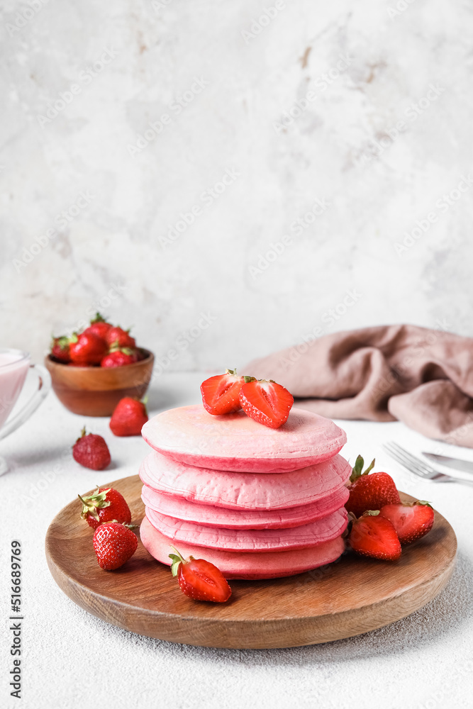 Wooden plate of tasty pink pancakes with strawberry on light background