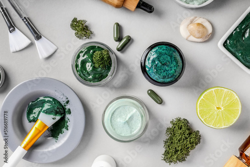 Composition with different jars of spirulina facial masks and ingredients on light background