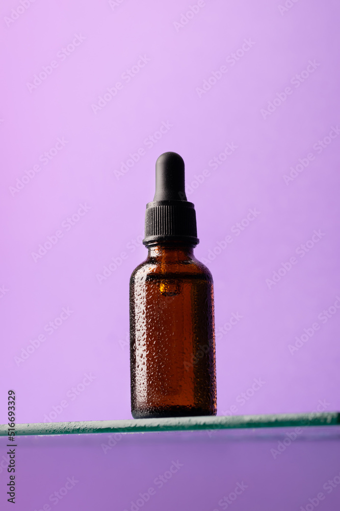 Bottle of cosmetic product, dark glass with pipette on glass shelf, purple background, looking up