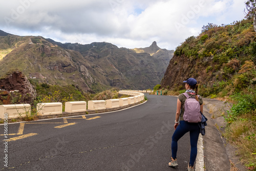 Hiking woman standing on empty curvy winding mountain road in the remote village of Afur on Tenerife, Canary Islands, Spain, Europe, EU. Panoramic view on mountain peak Roque de Taborno, Anaga massif